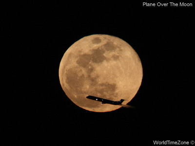 A plane flies in front of the Moon by worldtimezone