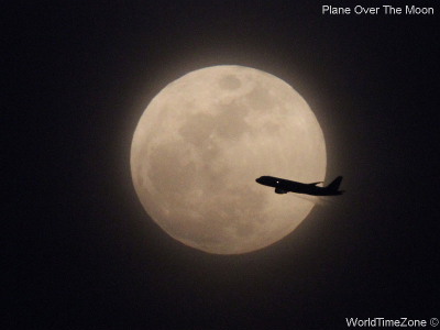 A plane flies in front of the Moon by worldtimezone